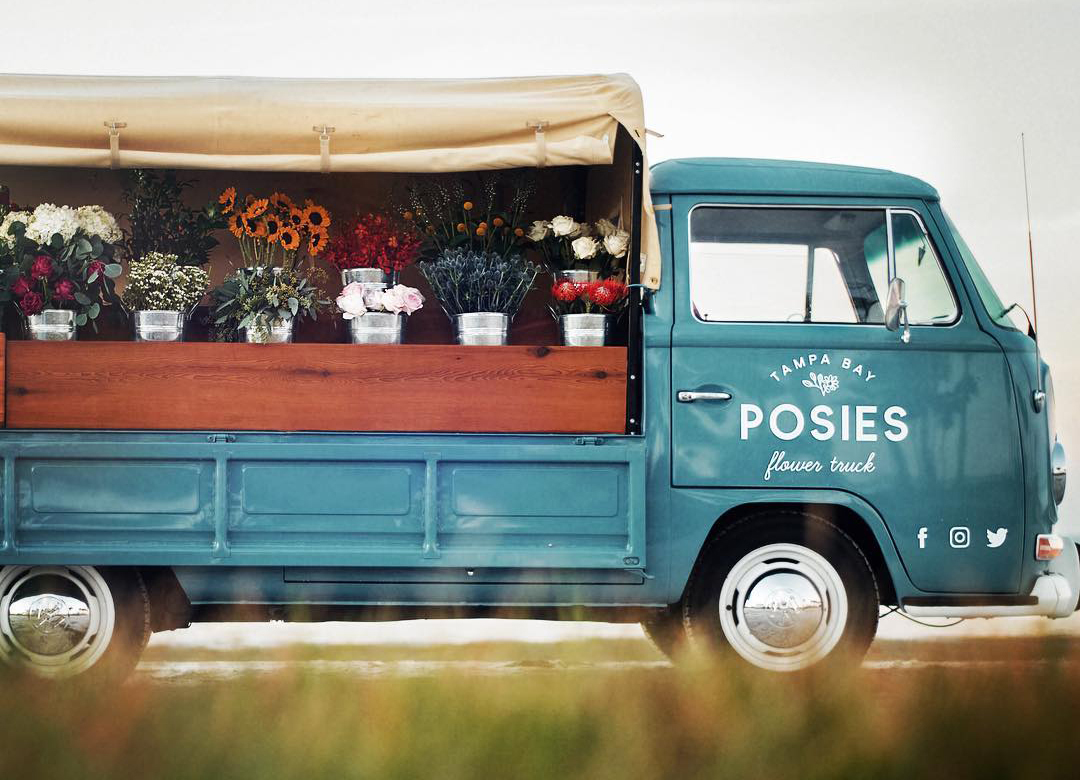A side photo of Posies Flower Truck. The truck has the canvas open and colorful flowers in each bucket.